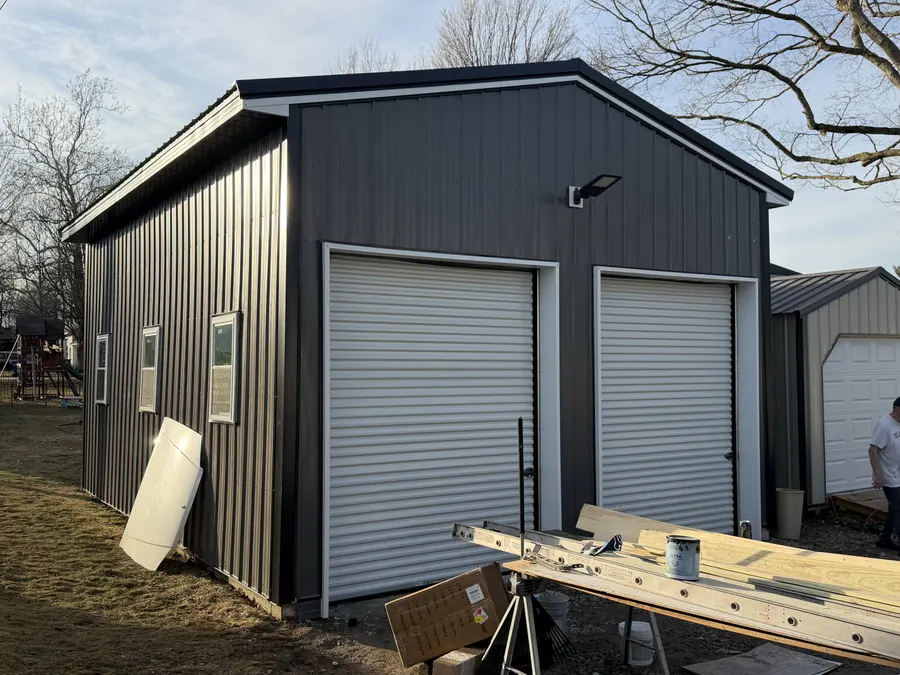 A finished black metal barn with white doors, photographed at dusk.