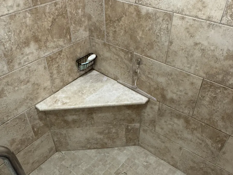 A finished walk-in shower tiled floor to ceiling, with a built-in corner shelf.
