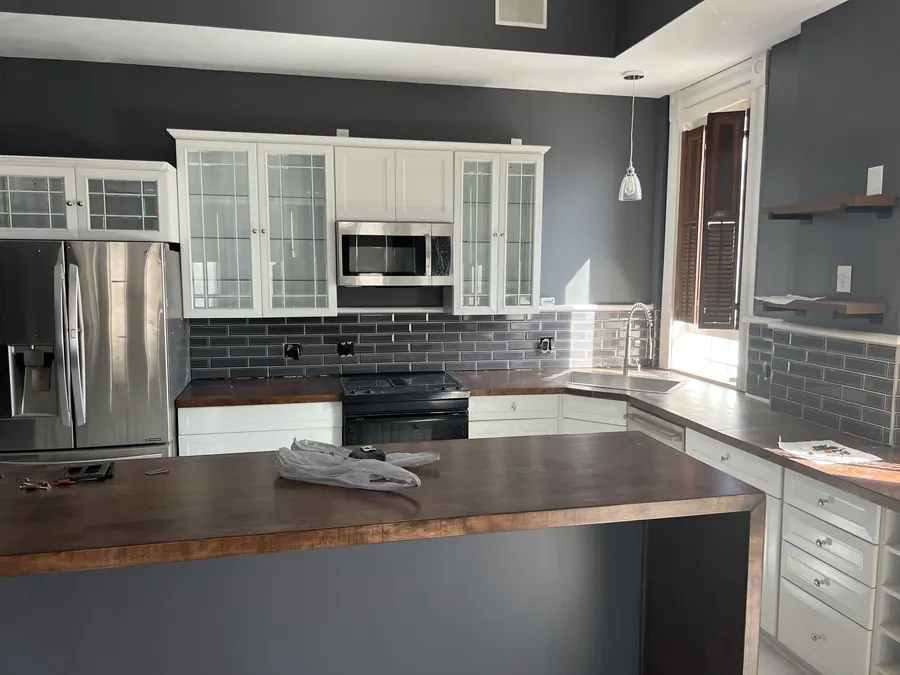 A kitchen remodeled by ZKB: new cabinets, a dark tile backsplash and a wood-top island.